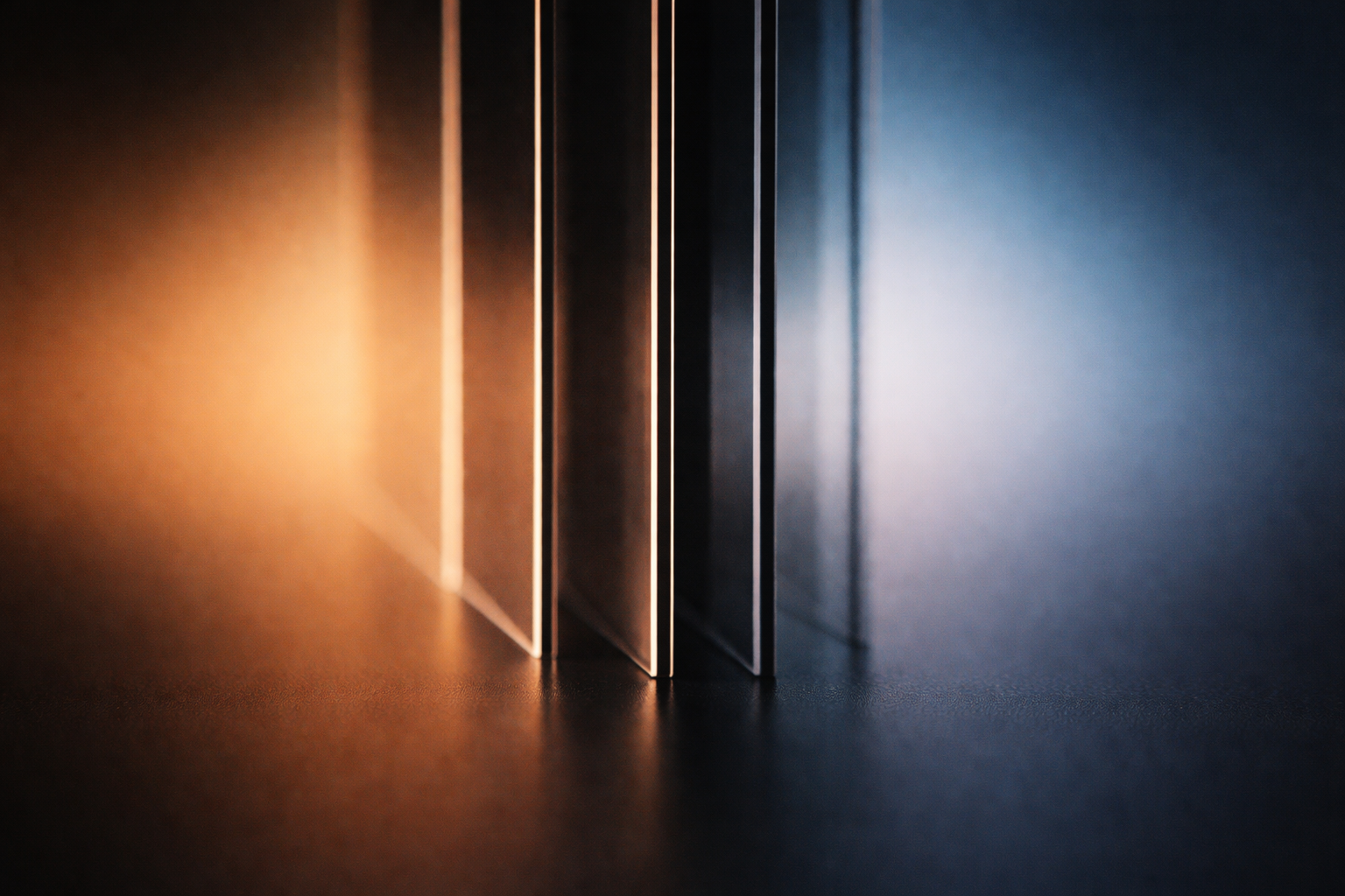 Macro silhouette of stacked translucent acrylic plates shown edge-on as dark vertical shapes against a warm amber-to-blue gradient backlight, centered in the upper two thirds with a quiet lower third.