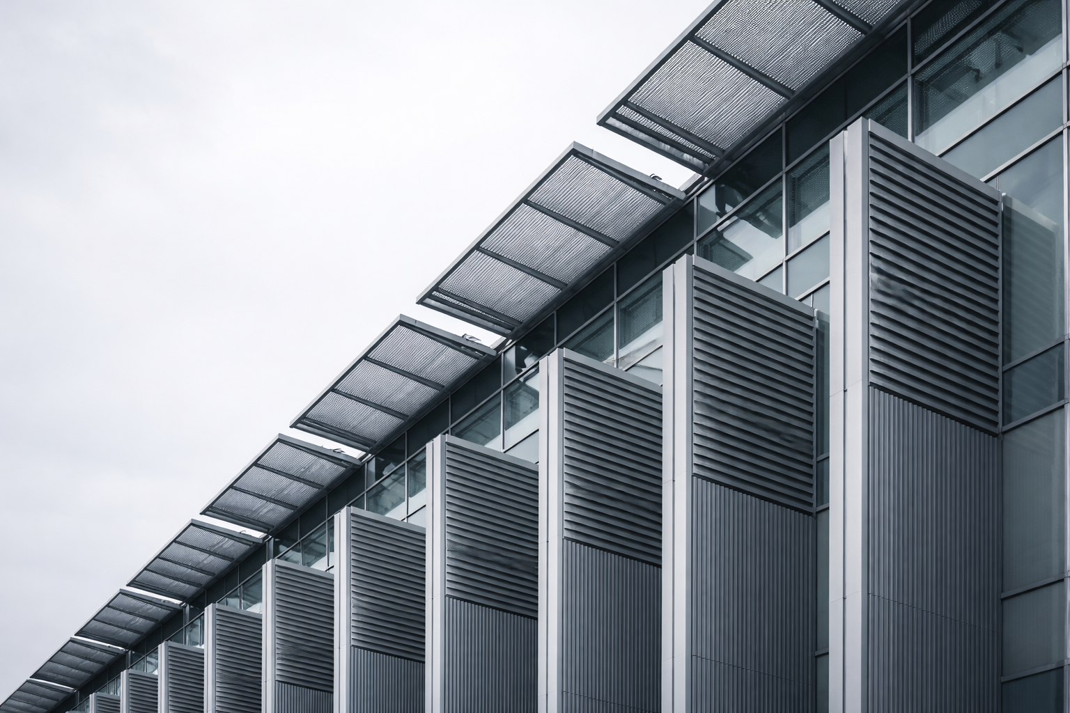 Low-angle view of repeating silver ventilation fins and sunshades on an unbranded research building against a soft gray-blue sky.