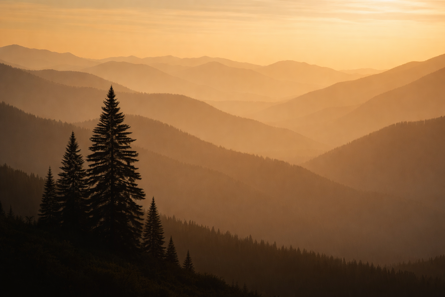 Silhouetted mountain ridges and a solitary tree fade into atmospheric haze under a warm, golden sky at dusk.
