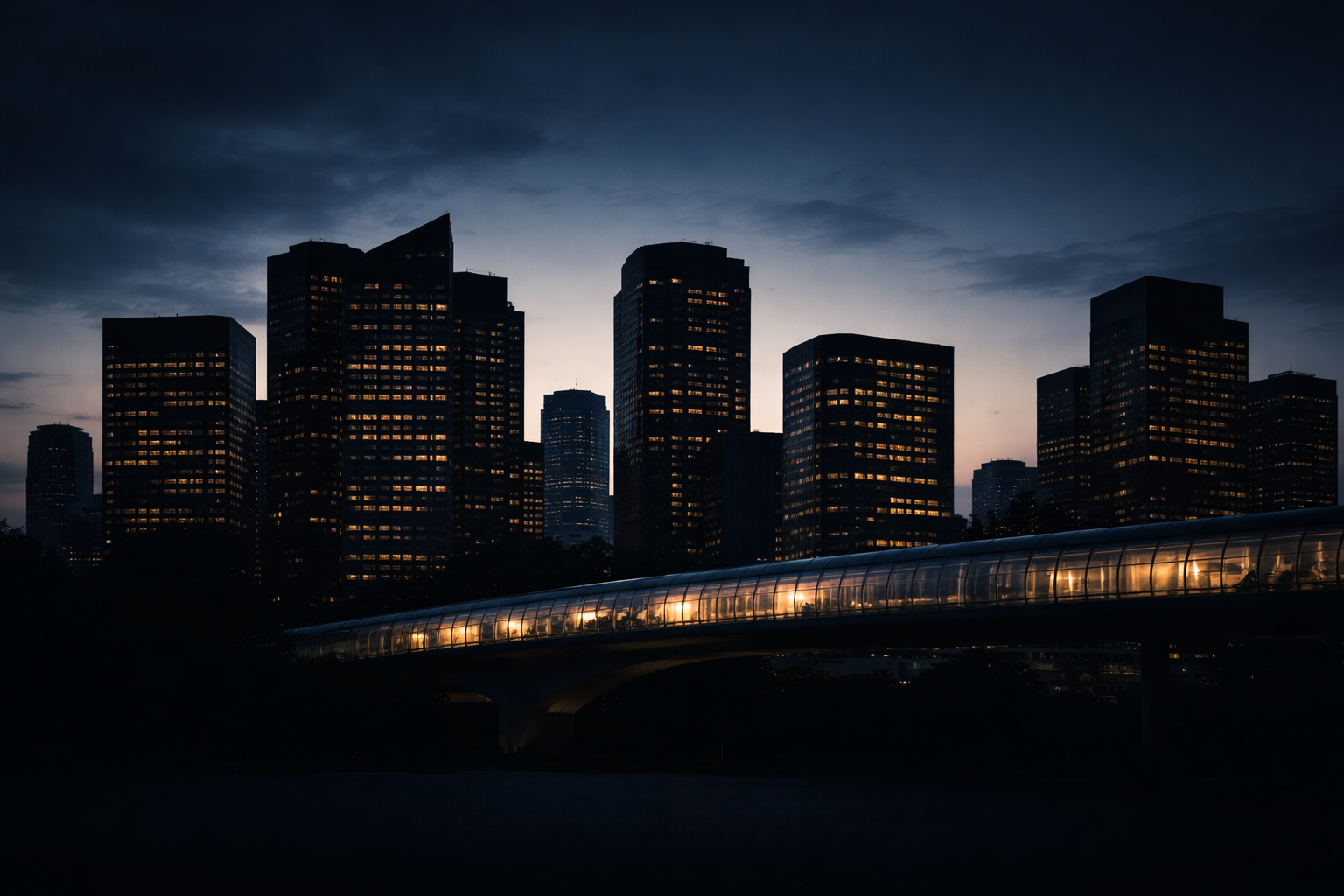 Dusk silhouette of anonymous modern office towers and a glass pedestrian bridge centered in frame, warm interior lights glowing against a deep indigo sky, with the lower third left dark and uncluttered.